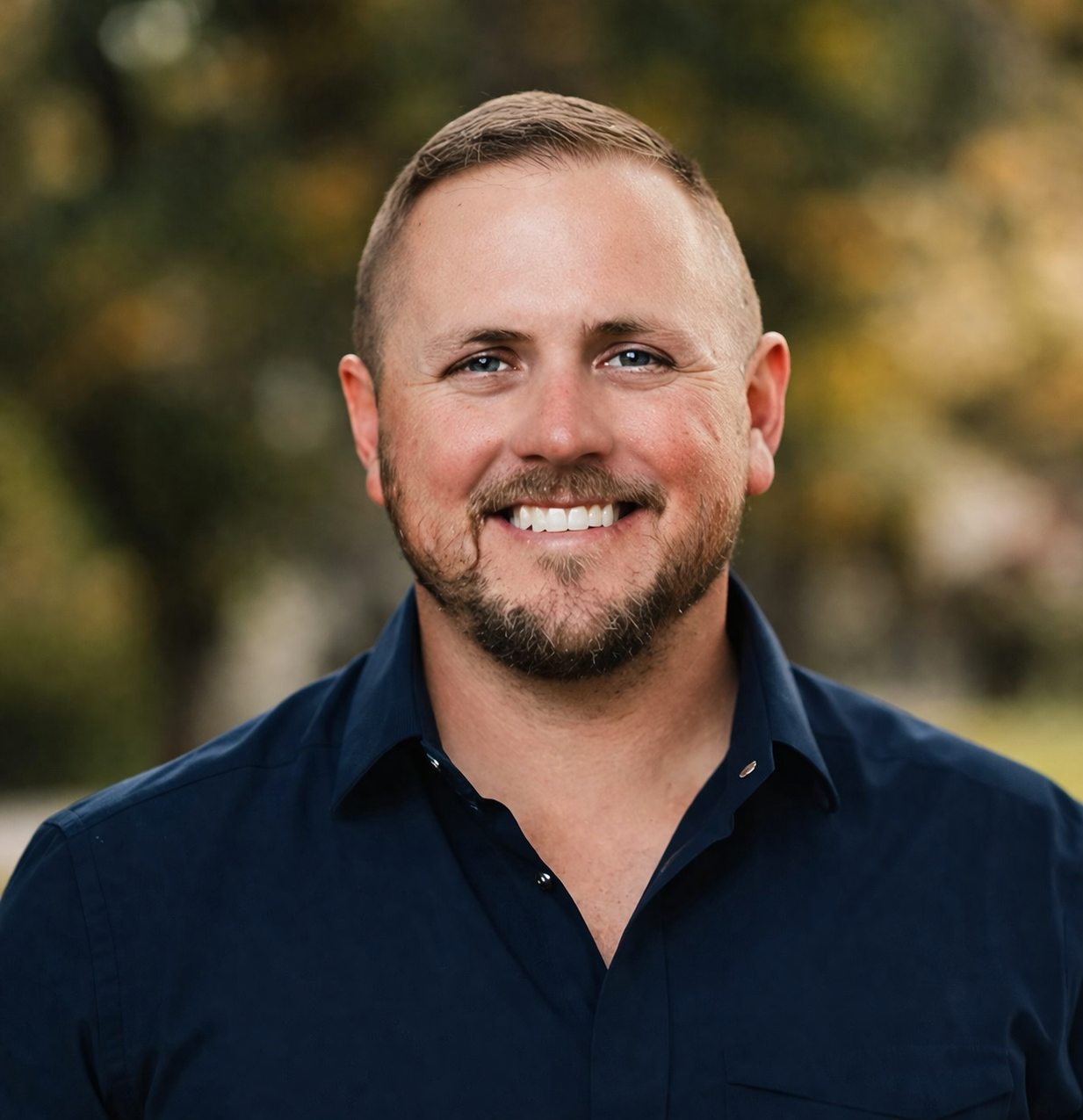 Smiling man with short hair wearing a dark blue shirt outdoors.